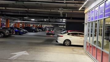 A multi-level underground parking garage with cars parked on various levels, visible structural beams, and a building with signage on the right.