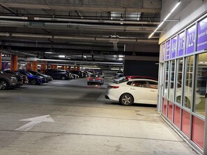 A multi-level underground parking garage with cars parked on various levels, visible structural beams, and a building with signage on the right.