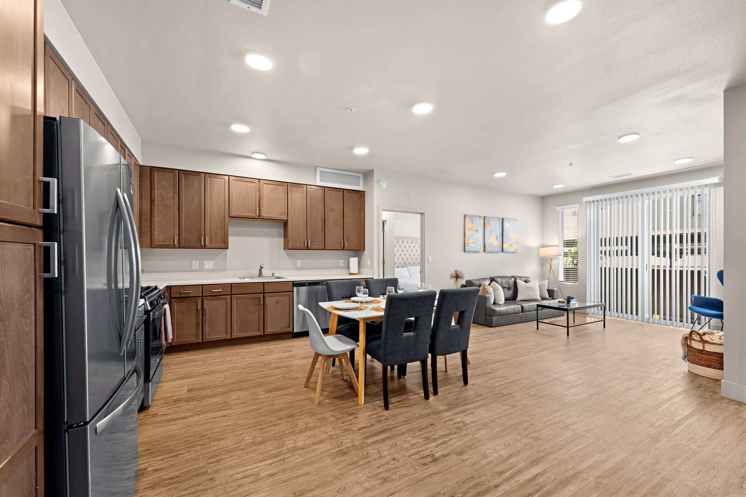 A modern kitchen with wooden cabinets, a stainless steel refrigerator, and a dining area with a table and chairs.