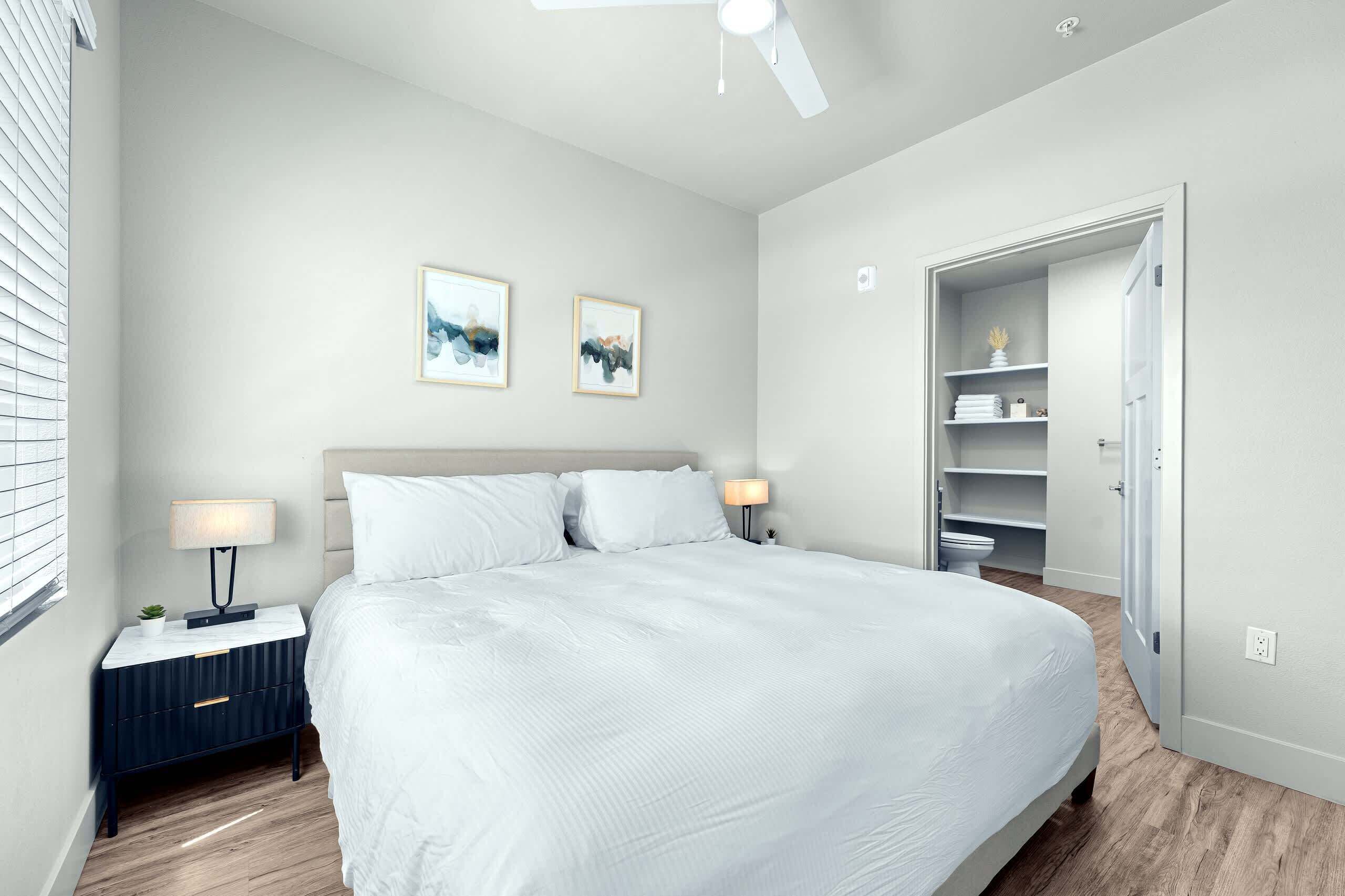A modern bedroom with a large bed, bedside lamps, a nightstand, and a closet with shelves.