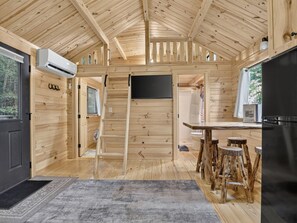 Interior de una cabaña de madera con cocina, comedor y una escalera que sube a un altillo.