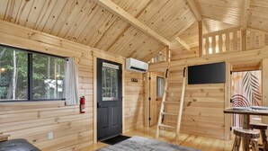 Interior de una cabaña con una puerta negra, un extintor, un ventanal, techo de madera y una alfombra gris.