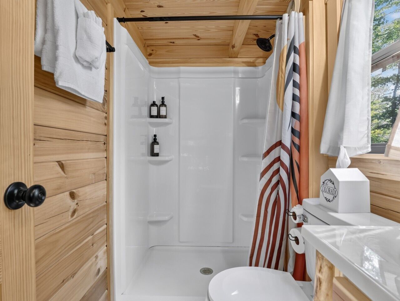 A compact bathroom with a shower, toilet, and a wooden wall.
