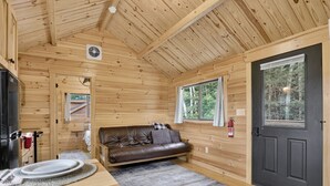 Interior de una cabaña de madera con mesa de comedor, sofá y puerta que da al exterior.