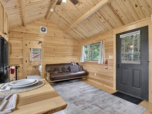 Ein Holzblockhaus-Innenraum mit Esstisch, Sofa und einer zur Außenseite führenden Tür.