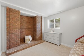 A bedroom with a brick fireplace, a white dresser, and a window with blinds. - Fantastic 2-bedroom apartment with AC in charming East Layton (Layton)