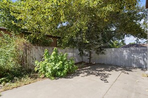 Ein durch einen Zaun eingemachter Garten mit einem Baum, einem kleinen Strauch und einer Betonauffahrt.