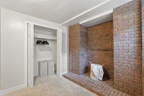 A room with a white door leading to a closet with hanging clothes, a brick fireplace, and a small step leading to a seating area. - Fantastic 2-bedroom apartment with AC in charming East Layton (Layton)