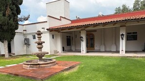 A building with a covered patio, a fountain, and a well-maintained lawn.