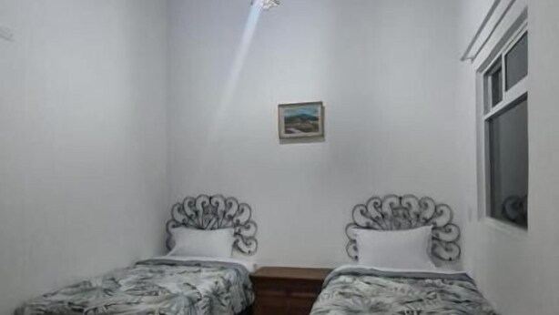 A room with two beds, a wooden ceiling, a single light fixture, and a window.