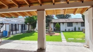 A covered outdoor area with a wooden ceiling, a concrete floor with pebble borders, and a view of a building with a tiled roof.