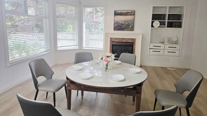 A dining room with a round table, six chairs, a fireplace, and a bookshelf. - Bright & Spacious Estate (Surrey)