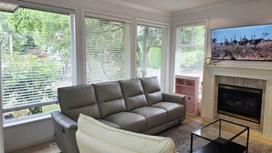 A living room with a grey sofa, a white armchair, a flat-screen TV, and a fireplace. - Bright & Spacious Estate (Surrey)