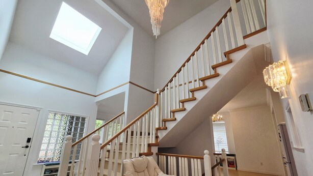 A spacious interior with a high ceiling, a staircase with wooden railings, and a chandelier. - Bright & Spacious Estate (Surrey)