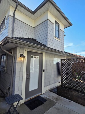 A two-story house with a grey door, a small porch with a bench, and a wooden fence. - Private Comfortable Guest House (Vancouver)