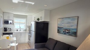 A modern kitchen with white cabinets, a black refrigerator, and a dining area with a white table and chairs. - Private Comfortable Guest House (Vancouver)