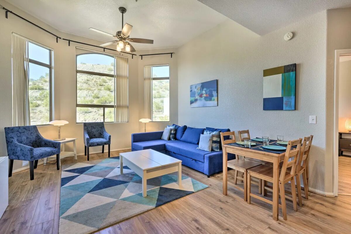 A spacious living area with a sofa, chairs, a coffee table, and a dining table with chairs. Large windows provide views of the outdoors.
