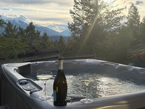 Un bain à remous avec une bouteille de vin et deux verres, entouré d’arbres et de montagnes.