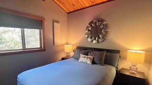 A bedroom with a bed, two bedside tables with lamps, a wall clock, and a window with blinds. - Invermere Getaway with Stunning Views and Hot Tub! (Invermere)