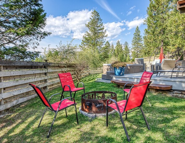 Un espace patio avec un foyer, des chaises rouges et un coin salon offrant une vue sur les arbres.