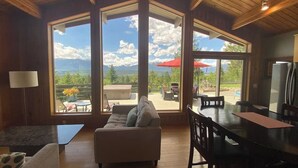 A spacious living area with a large window, a sofa, a dining table, and a kitchen area. - Invermere Getaway with Stunning Views and Hot Tub! (Invermere)