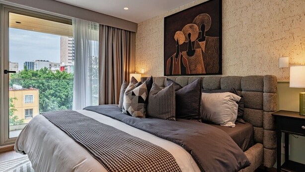 A modern bedroom with a large bed, a city view, and a contemporary abstract painting. - 3 Private Apts in Condesa with Private Terrace (Mexico City)