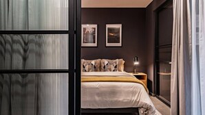 Ein Schlafzimmer mit einem Bett, einem Nachttisch, zwei gerahmten Bildern und einem Fenster mit Vorhängen.