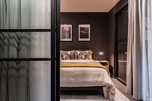 Ein Schlafzimmer mit einem Bett, einem Nachttisch, zwei gerahmten Bildern und einem Fenster mit Vorhängen.