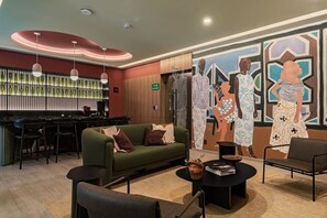 Un vestíbulo moderno con una zona de bar, un sofá verde y un mural con figuras abstractas.