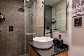 Un baño moderno con un lavamanos grande blanco, un box de ducha de vidrio y un espejo con una toalla colgada en la pared.