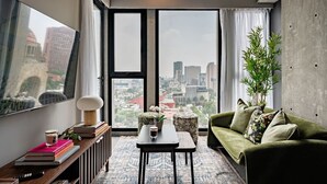 A modern living room with a large window, a green sofa, a coffee table, and a bookshelf. - Stylish Stay Across from Monumento a la Revolución (Mexico City)