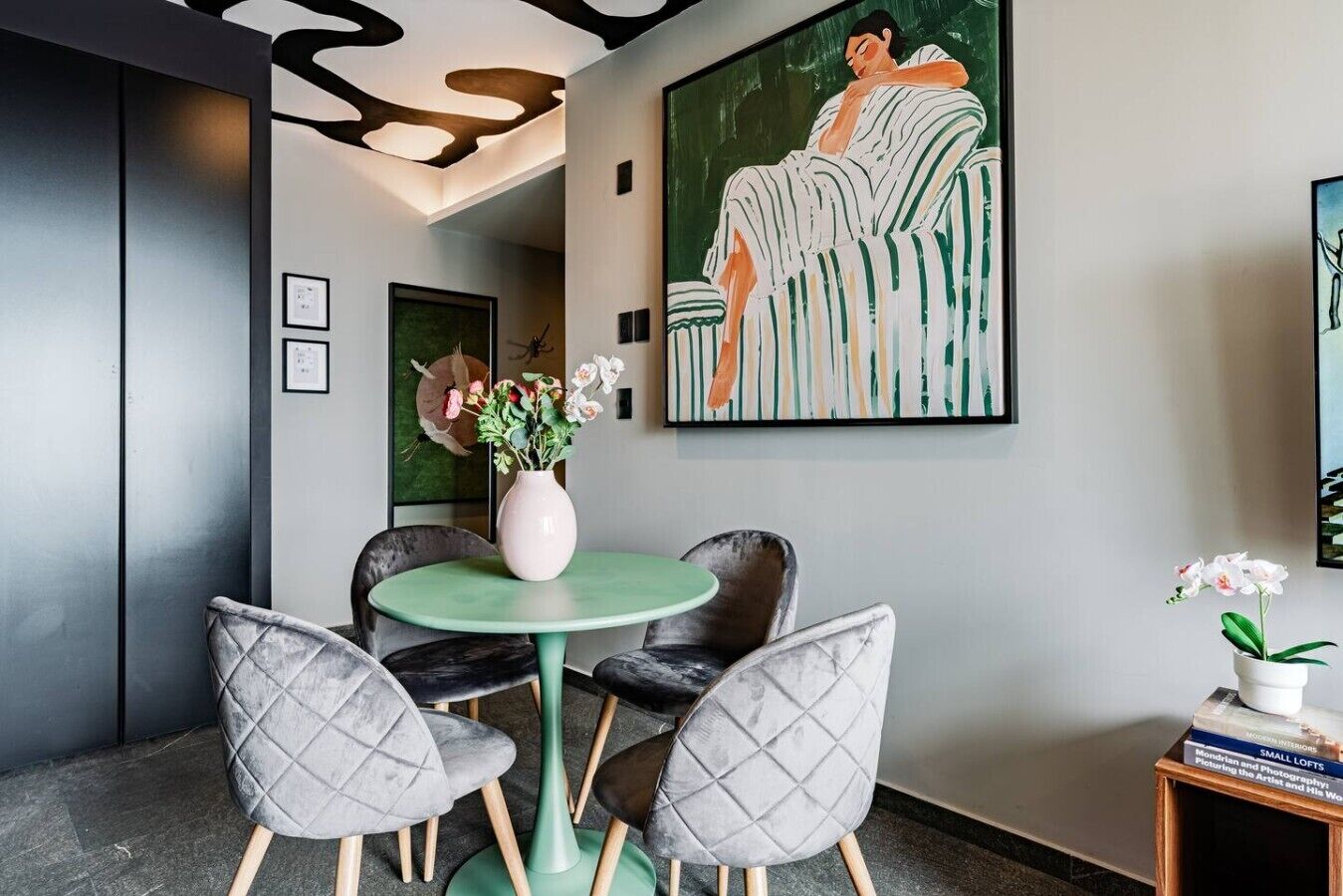 Um interior moderno com uma mesa redonda, duas cadeiras, um vaso com flores e uma grande pintura abstrata na parede.
