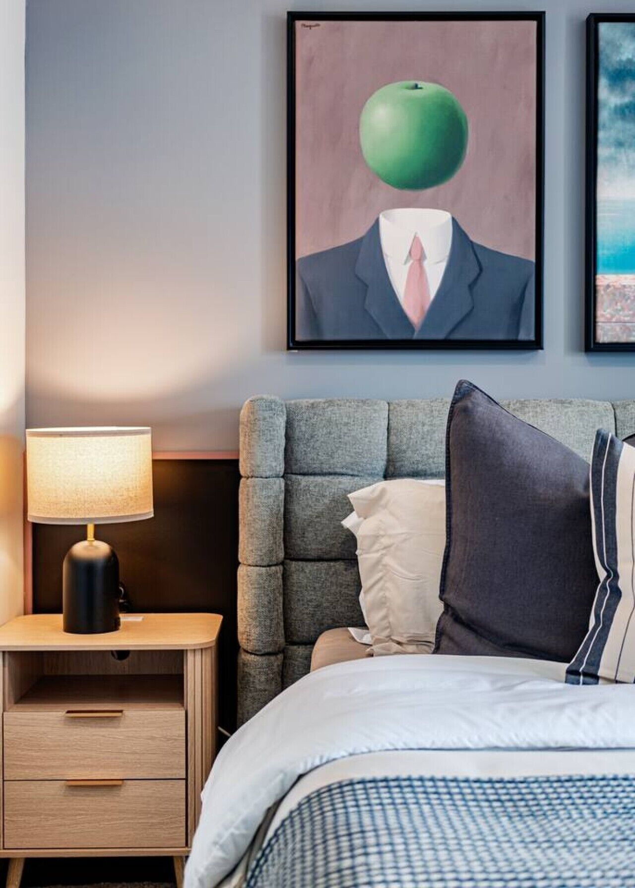 A bedroom with a bed, a nightstand with a lamp, and a painting on the wall.