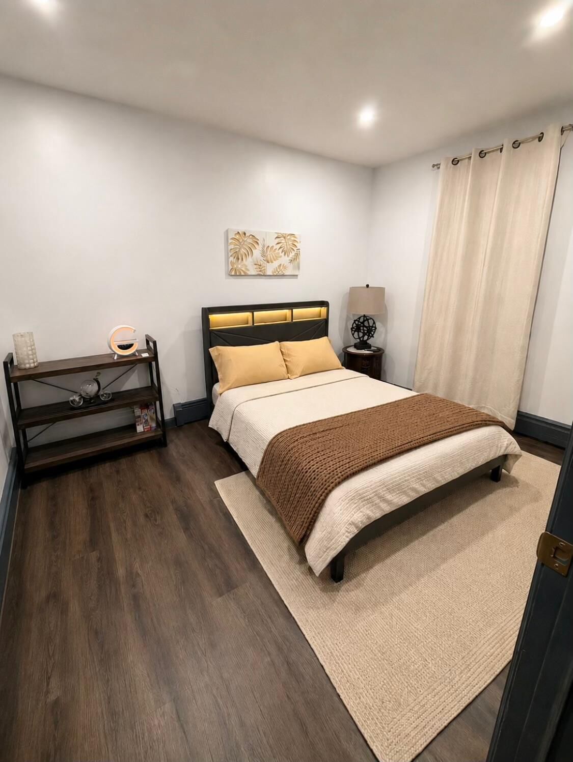 Un dormitori ordenat amb un llit, taules de nit, una làmpada i un element decoratiu a la paret.