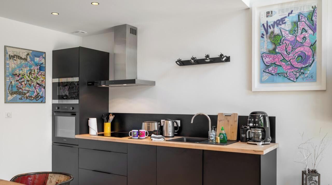 Uma cozinha moderna com um exaustor de aço inoxidável, uma máquina de café e uma pia.