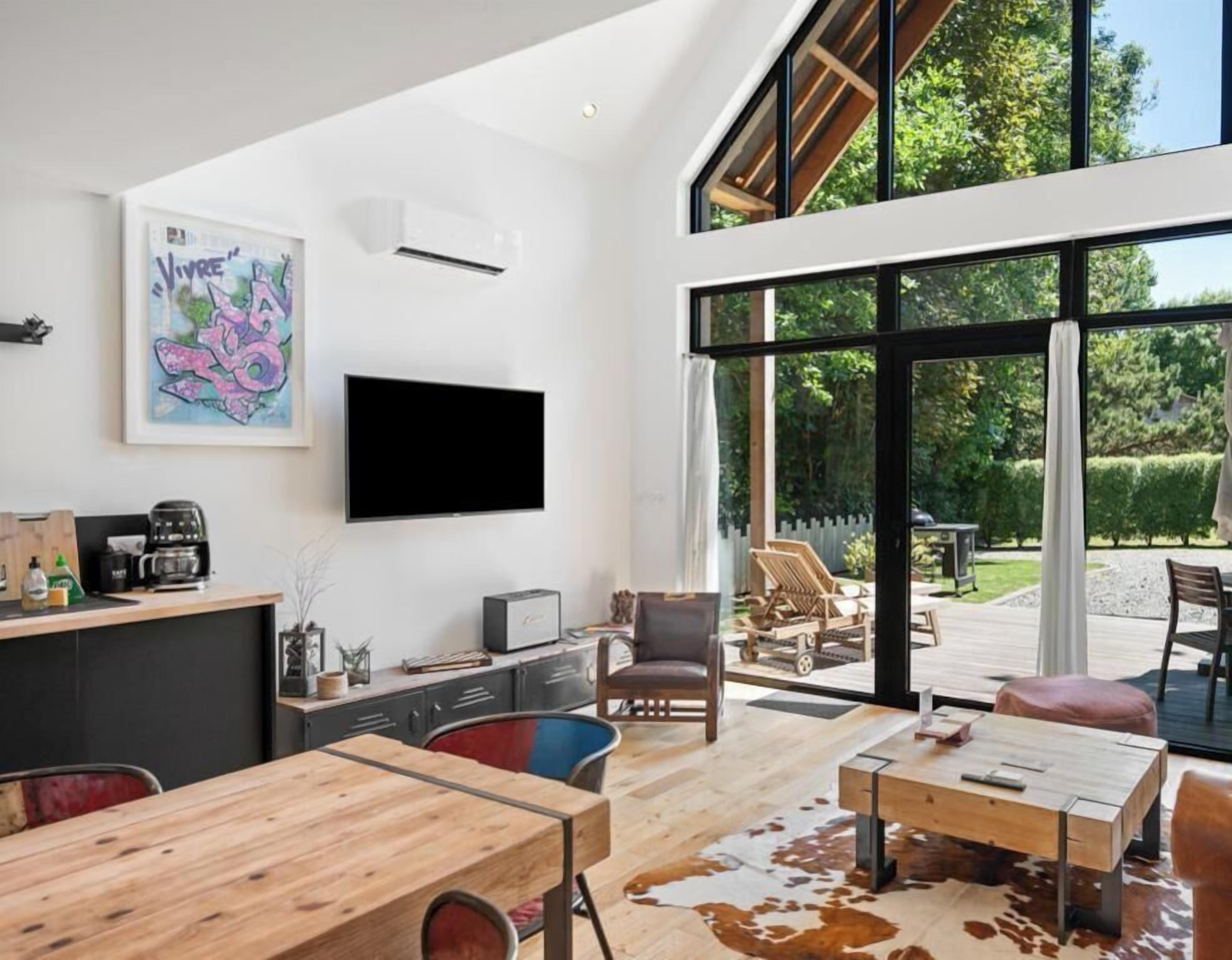 Een moderne woonkamer met een flatscreen televisie, houten meubels en een grote glazen schuindeur die uitkomt op een terras.