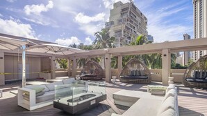 Eine Dachterrasse mit moderner Sitzgelegenheit, einem Tisch mit Glasplatte und Blick auf Palmen und Gebäude.
