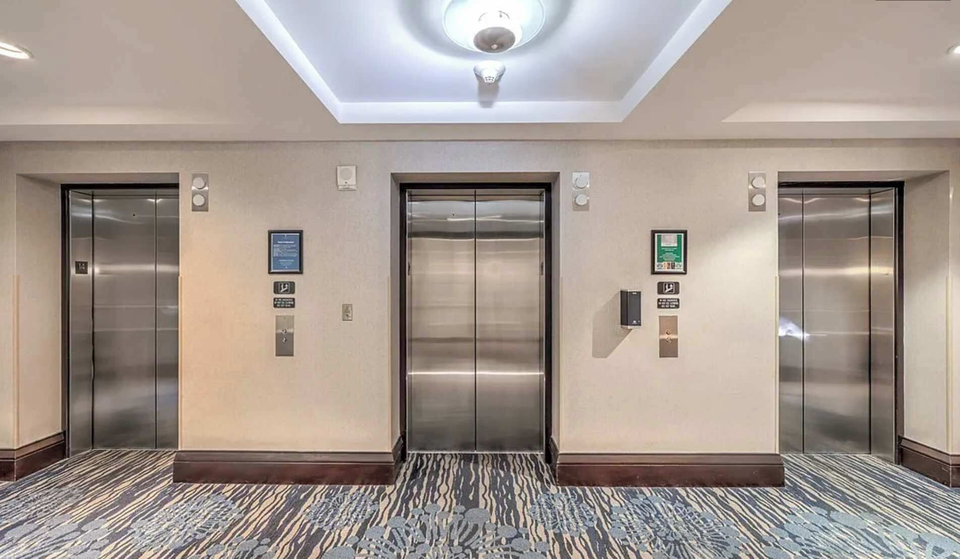 A hallway with three elevators, each with a control panel and a sign above.