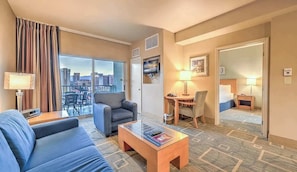 A hotel room with a sofa, a coffee table, a TV, a desk with a chair, and a city view through the window. - Spacious Vegas Strip View Balcony Full Kitchen (Las Vegas)