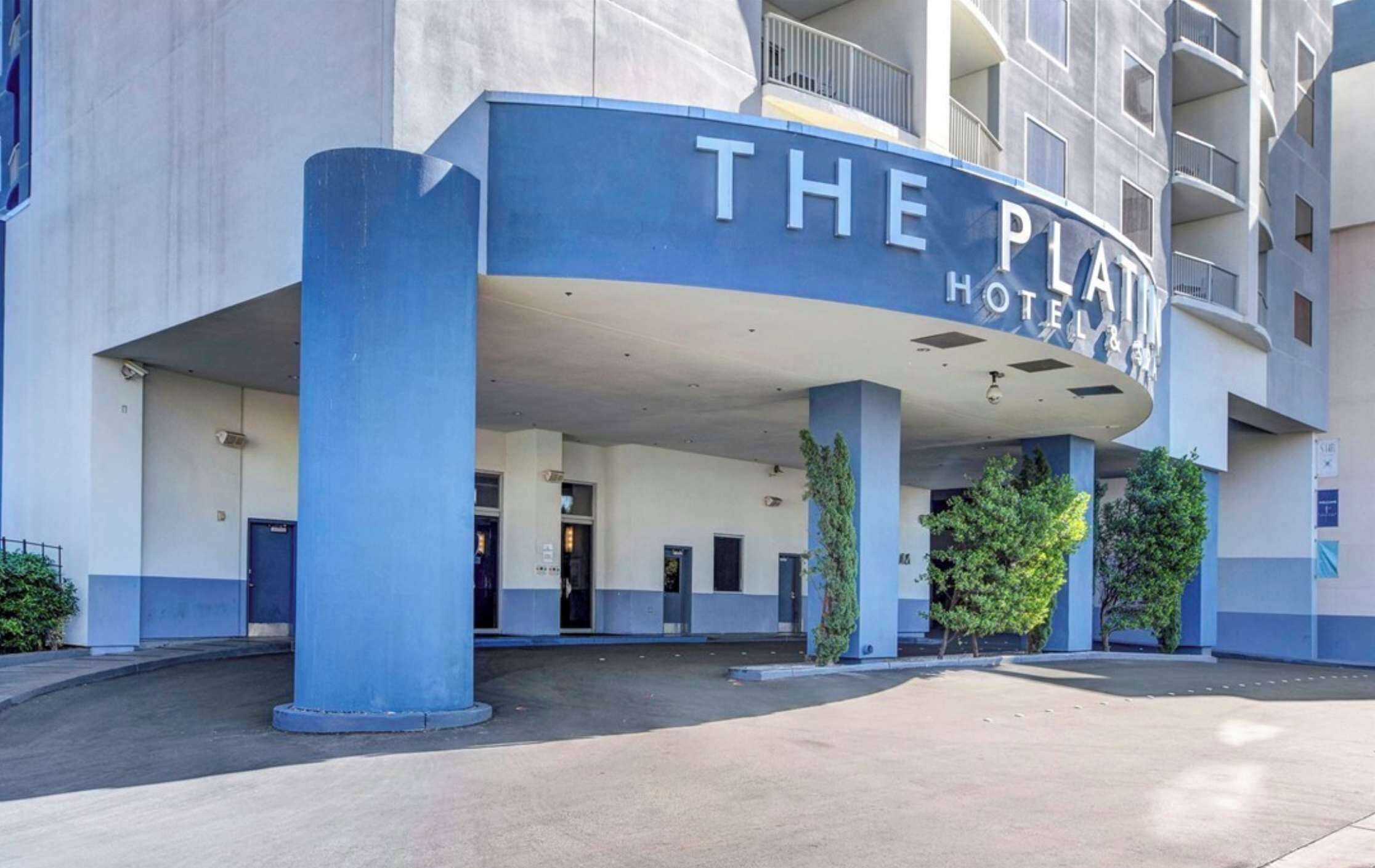 A hotel entrance with a blue and white facade, multiple doors, and a covered area.