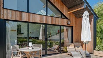 A modern wooden building with large glass windows, outdoor seating, and a patio area.