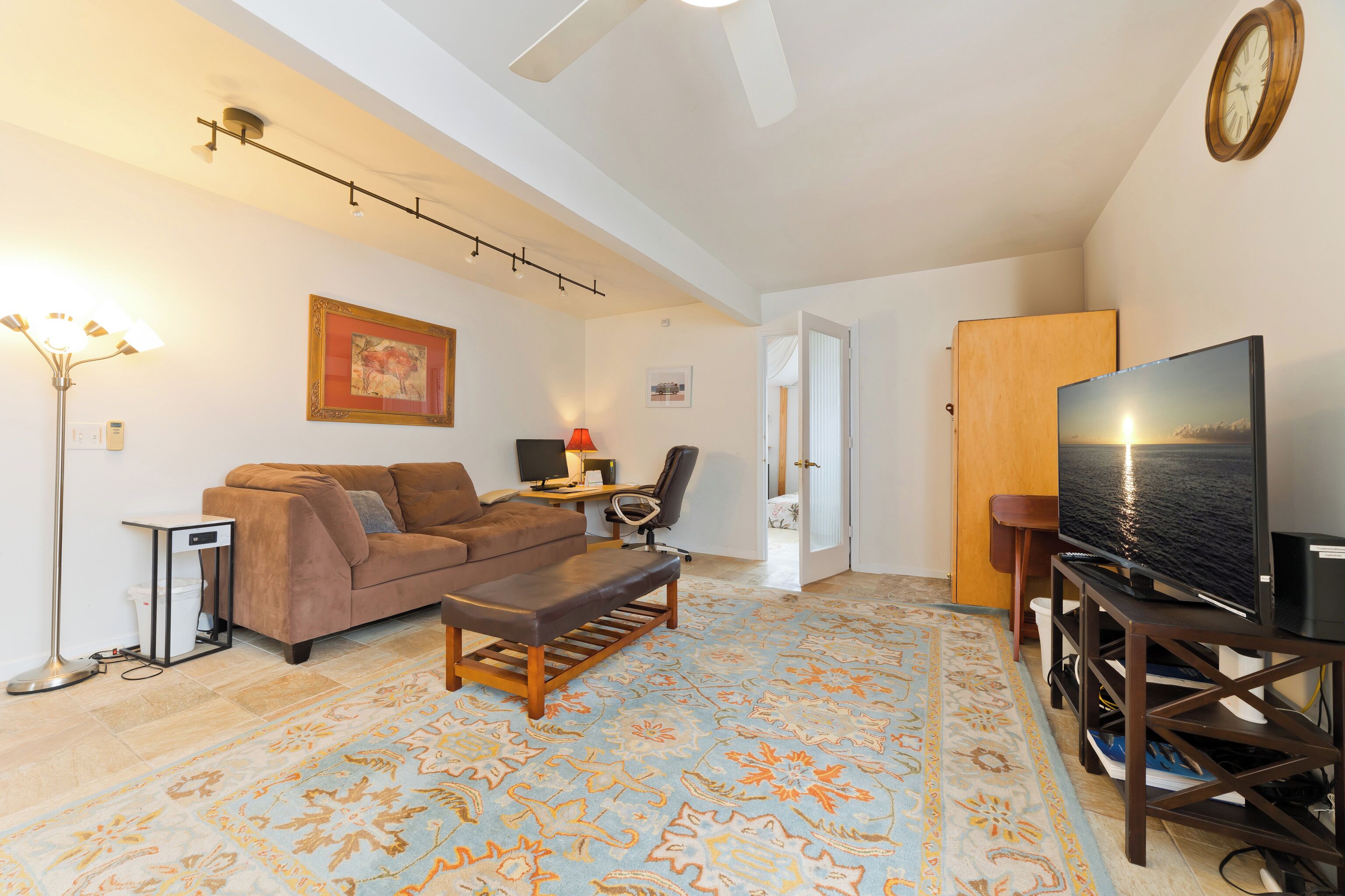 A living room with a sofa, a coffee table, a TV on a stand, a lamp, and a patterned rug.