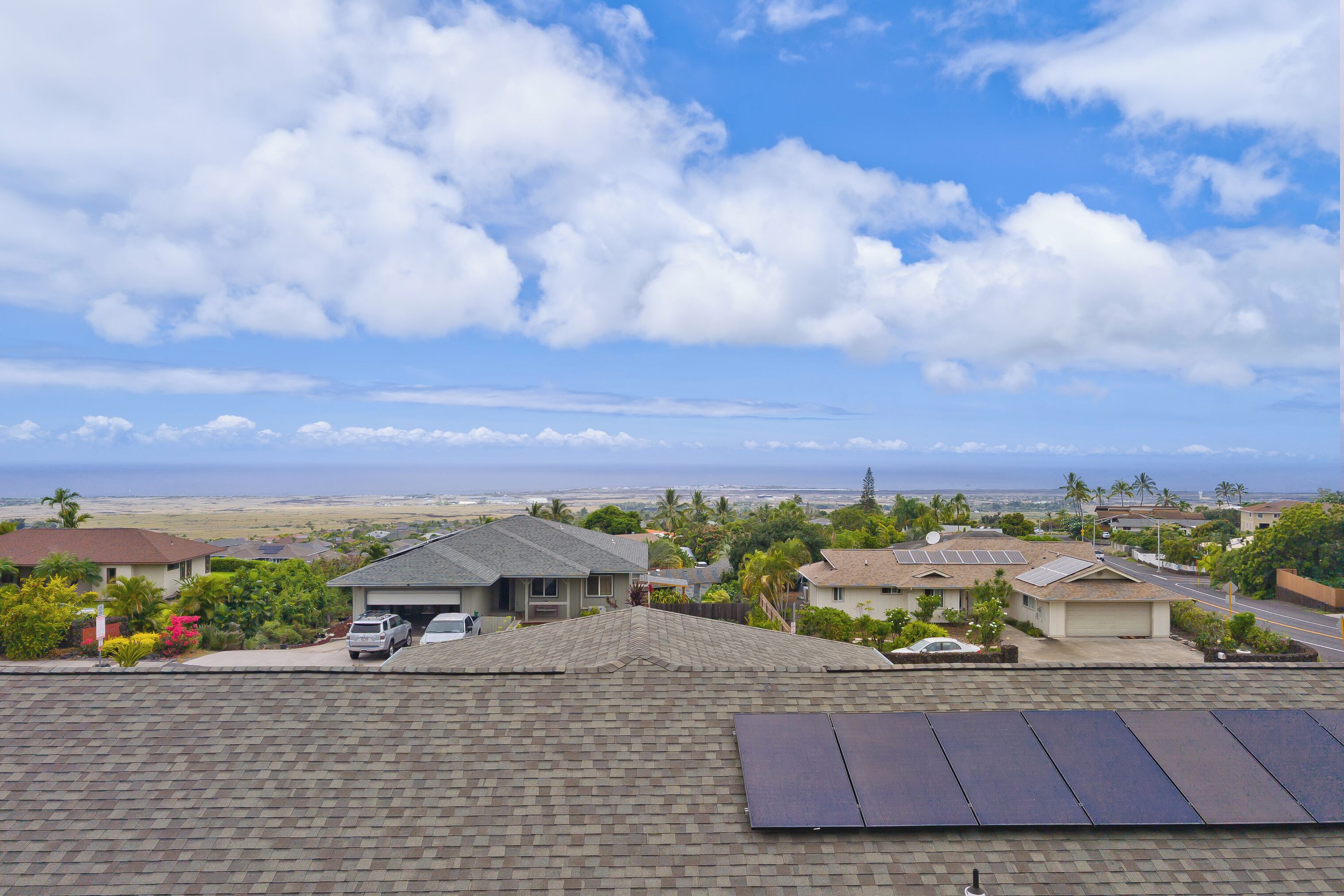 A residential area with houses, solar panels on rooftops, and a view of the ocean.