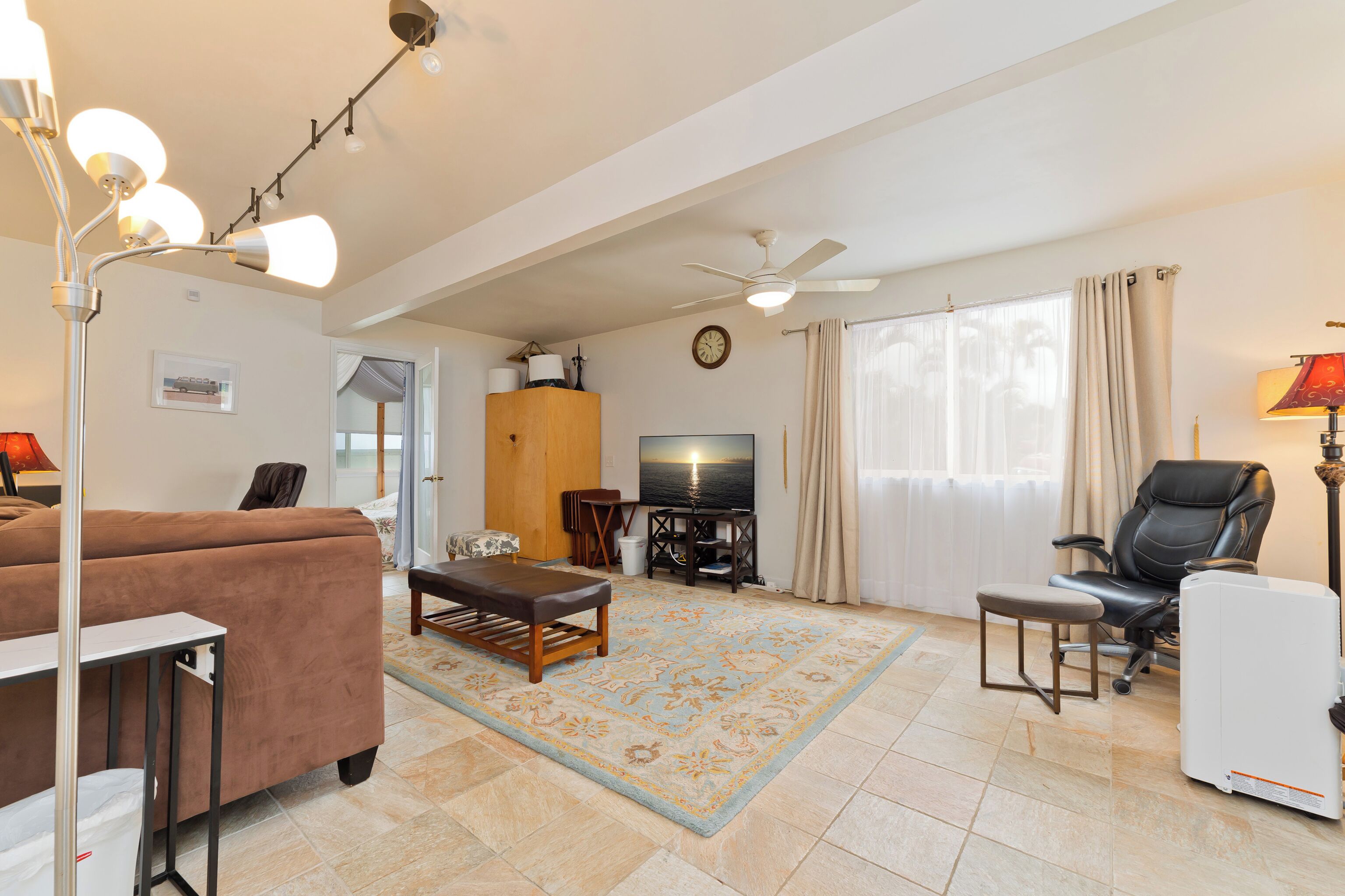 A living room with a sofa, a coffee table, a TV, a ceiling fan, and a window with curtains.