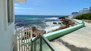 A coastal view with a balcony, rocky shoreline, and a building with a modern design. - Oceanfront Suite - Excellent Location - Altamar (Isla Mujeres)