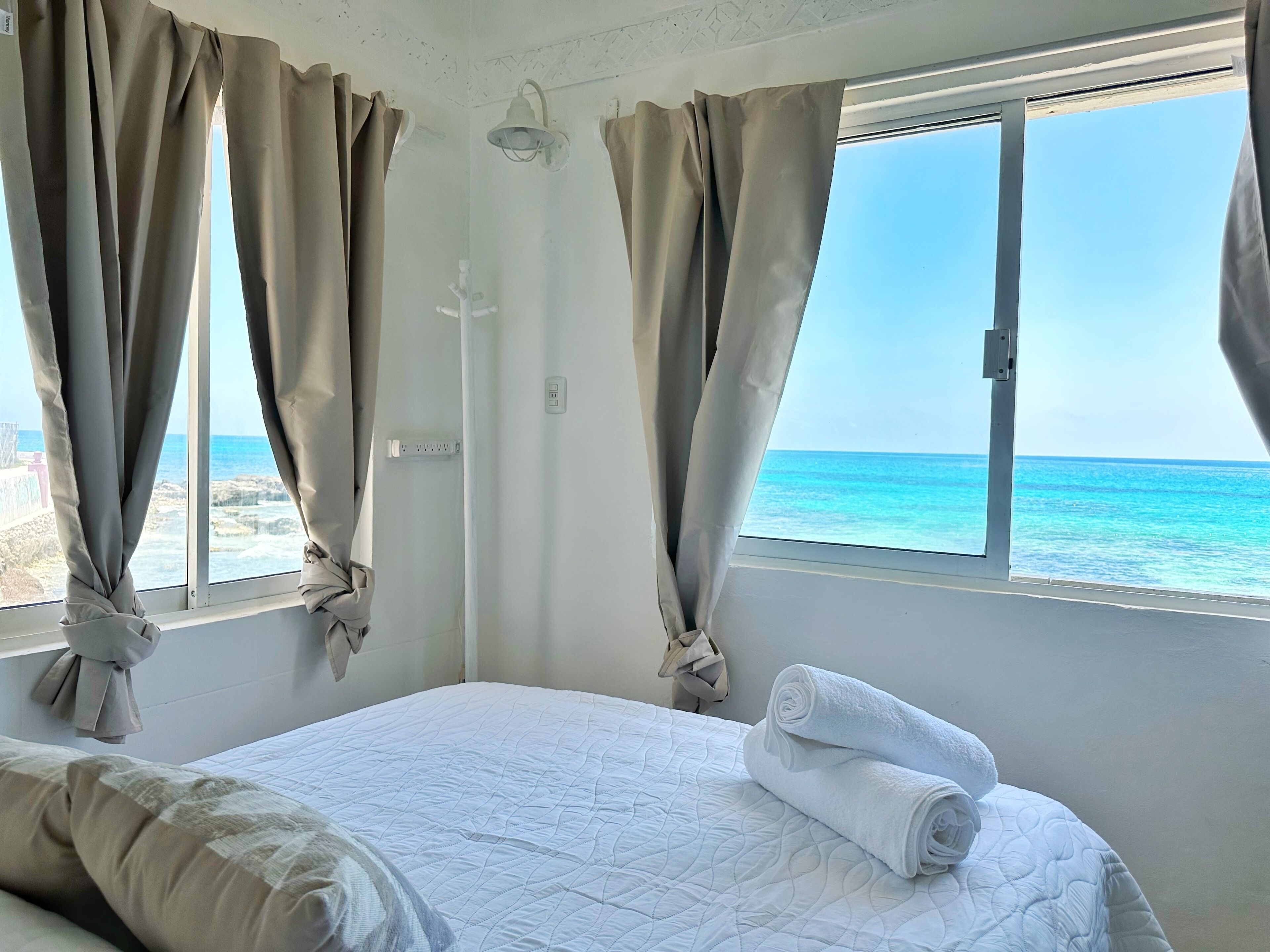 Une chambre avec un lit, des rideaux, une fenêtre et une vue sur l’océan.