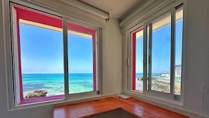 A corner room with a wooden desk, two white chairs, and large windows with red frames. - Oceanfront Suite - Excellent Location - Altamar (Isla Mujeres)