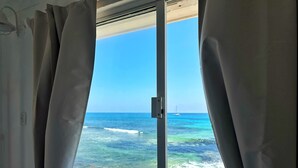 A window with curtains, a view of the ocean, and a sailboat in the distance. - Oceanfront Suite - Excellent Location - Altamar (Isla Mujeres)
