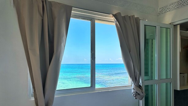 A room with a window overlooking the ocean, a bed with a rolled towel, and a green door. - Oceanfront Suite - Excellent Location - Altamar (Isla Mujeres)