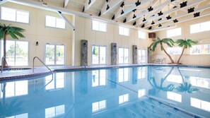 En indendørs swimmingpool med krystalklart vand, stensøjler og palmer.